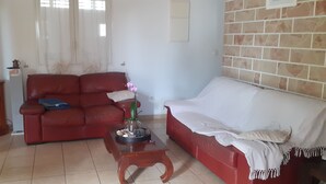 A living room with a red sofa, a white sofa, a wooden coffee table, and a television on a stand. - La Kaz Thomas (Saint-Leu)