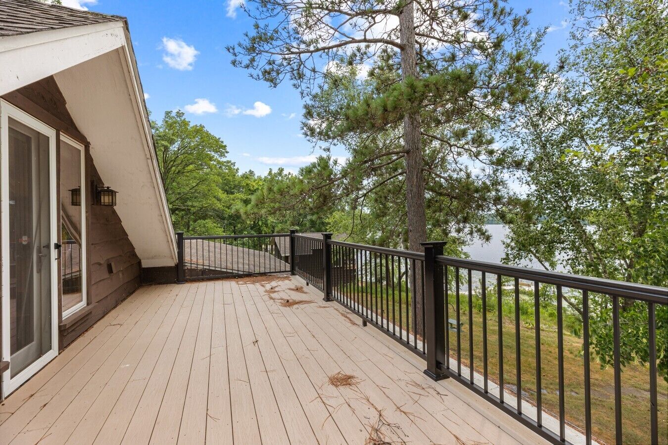 A wooden deck with a black railing, overlooking a body of water and surrounded by trees.
