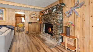Interior acollidor d'una cabana amb una llar de pedra, parets de fusta, zona de dinar i saló amb sofà.