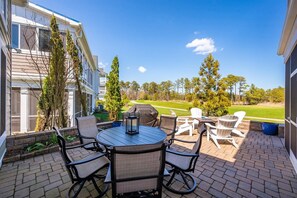 Un patio con un tavolo rotondo e sedie, un barbecue e vista su un campo da golf.