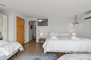 A hotel room with two beds, a wooden door, a small bedside table with a lamp, a blue patterned rug, and a staircase leading to an upper level. - Cozy Rice Lake Cabin w Balcony, Grill & Views (Brainerd)