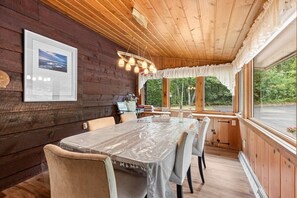 A wooden interior with a dining table, chairs, a framed picture, and a window with a view of greenery. - Lakefront Brainerd Cabin w Deck, Fire Pit! (Brainerd)