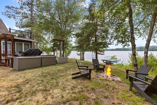 A backyard with a fire pit, outdoor seating, and a view of a lake.