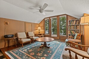 A cozy room with a large window, a ceiling fan, a round table, and a bookshelf. - Lakefront Brainerd Cabin w Deck, Fire Pit! (Brainerd)