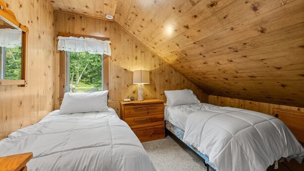 A bedroom with two beds, a window with a white valance, a bedside lamp, and a wooden ceiling. - Lakefront Brainerd Cabin w Deck, Fire Pit! (Brainerd)