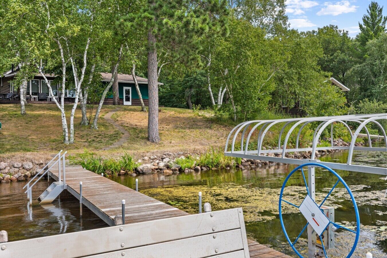 A wooden dock leading to a small pond with a metal railing and a control wheel.