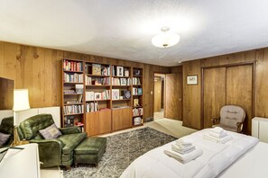 Une pièce comprenant un lit, un fauteuil en cuir vert, une bibliothèque et une armoire en bois.