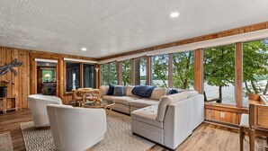 A spacious living area with a large window overlooking a body of water, furnished with a sofa, armchairs, and a coffee table. - Lakefront Brainerd Cabin w Deck, Fire Pit! (Brainerd)