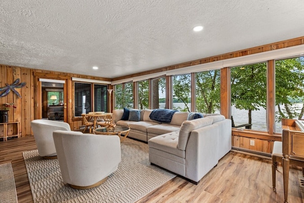 A spacious living area with a large window overlooking a body of water, furnished with a sofa, armchairs, and a coffee table.