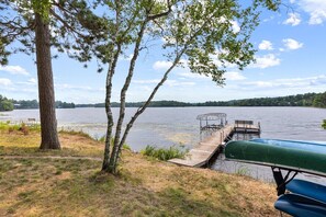 A lakeside dock with a bench and a covered area, surrounded by trees and a grassy area.