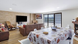 Una sala de estar moderna con un televisor de pantalla plana, una chimenea, una mesa de comedor con mantel estampado y un ventanal con vistas.
