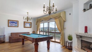 Una habitación con mesa de billar, sofá, candelabro y chimenea.