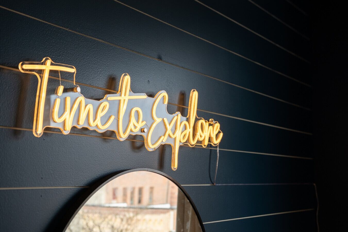 A neon sign that reads "Time to Explore" on a dark wall.