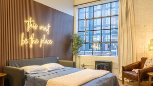 Un dormitorio moderno con cama, un letrero de neón, una ventana y una chimenea.