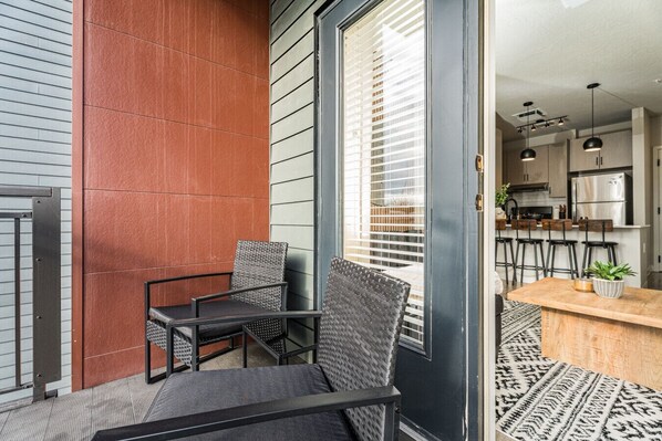 A modern kitchen with stainless steel appliances, a bar area with stools, and a sliding glass door leading to an outdoor seating area with two chairs.