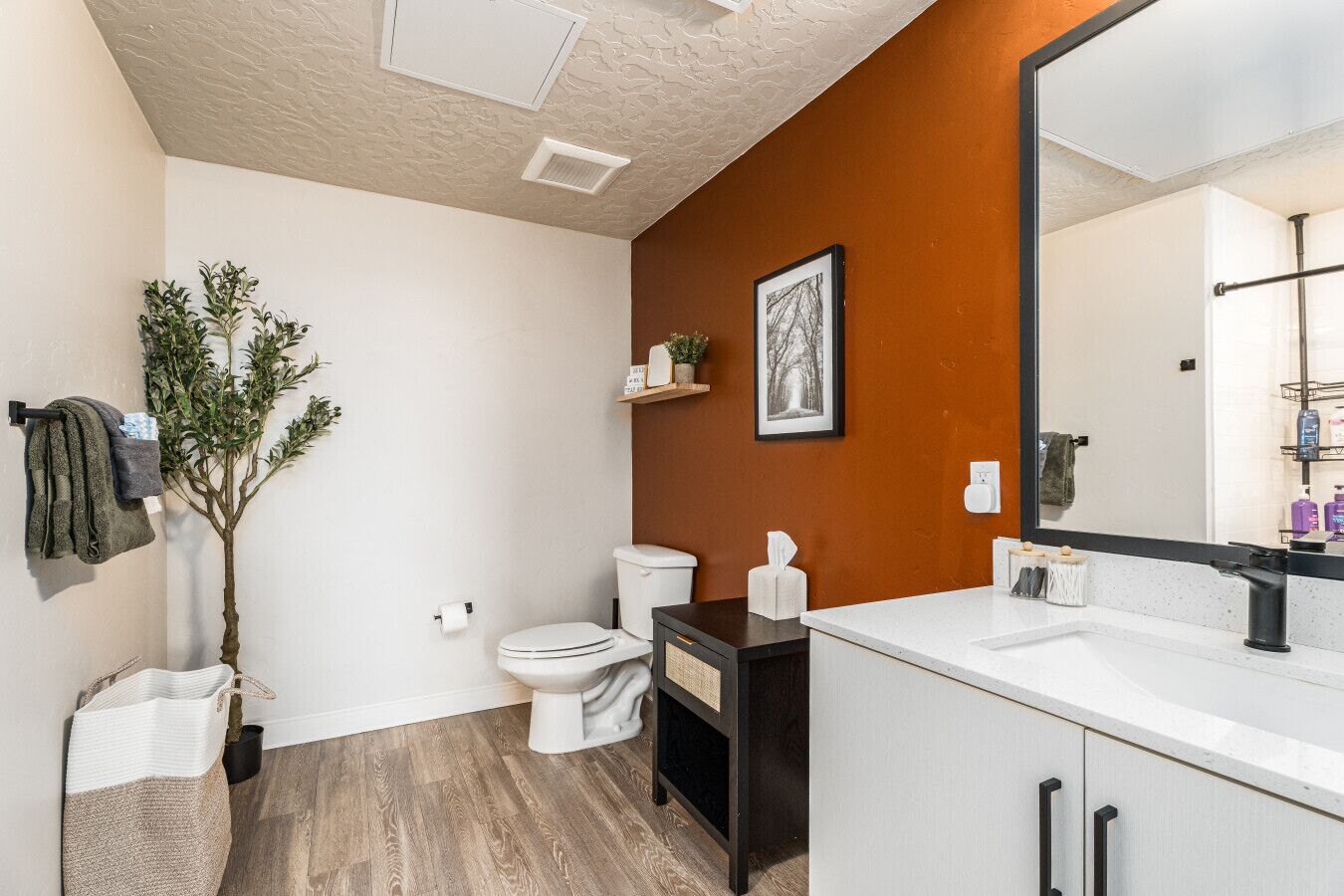 Un baño moderno con inodoro blanco, tocador negro y un espejo grande.