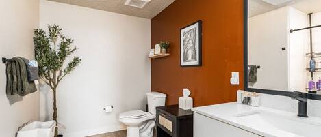 Un baño moderno con inodoro blanco, tocador negro y un espejo grande.