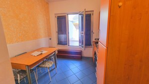 A small kitchen with a wooden table and chairs, a window with curtains, and a door. - Blue Bilo with terrace facing the sea and beach (Marcelli)
