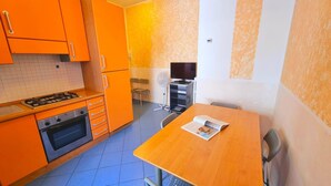 A compact kitchen with orange cabinets, a stove, and a small dining table with a newspaper. - Blue Bilo with terrace facing the sea and beach (Marcelli)