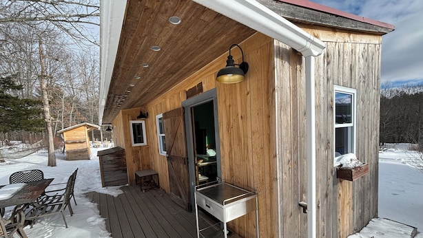 Puuinen mökki, jossa on terassi, pieni kuisti ja ulkokalusteilla varustettu ruokailutila.