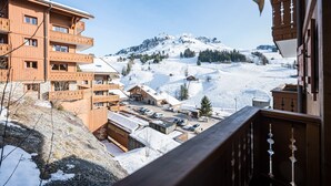 Ein Holzbauten mit mehreren Balkonen mit Blick auf eine verschneite Berglandschaft.
