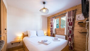 Ein gemütliches Holzhütten-Zimmer mit Bett, einem kleinen Nachttisch mit Lampe, einem Fenster mit Vorhängen und einer Heizung.
