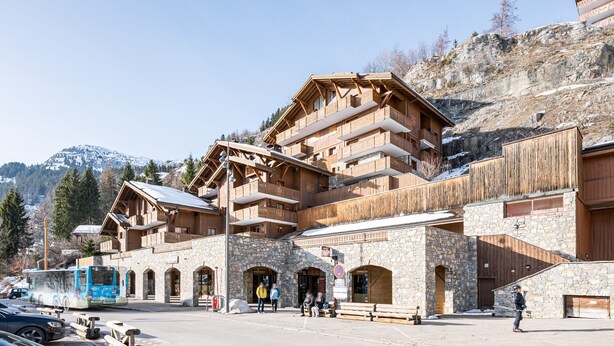 Ein Chalet im Holzbau mit Steinfassaden, mehreren Balkonen und einer Seilbahn im Hintergrund.