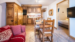Ein gemütliches Wohnzimmer mit einer rot-weiß karierten Couch, einem Holzespeisetisch und Stühlen. Im Hintergrund ist eine Küche mit Holzschränken und einer gefliesten Spritzschutzleiste zu sehen.