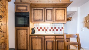 Eine Küche mit Holzausstattung, einem schwarzen Backofen, einer gefliesten Spritzschutzwand und einem Esstisch mit Stühlen.