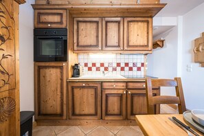 A kitchen with wooden cabinets, a black oven, a tiled backsplash, and a wooden dining table with chairs. - Village Lessy - Apt. O6 - Proche Station Ski (Le Grand Bornand)