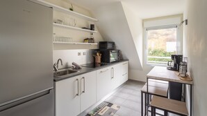 Eine moderne Küche mit weißen Schränken, einem Edelstahlkühlschrank, einer Mikrowelle und einer Kaffeemaschine auf einem kleinen Tisch.