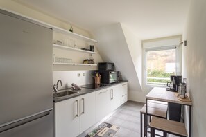 Eine moderne Küche mit weißen Schränken, einem Edelstahlkühlschrank, einer Mikrowelle und einer Kaffeemaschine auf einem kleinen Tisch.