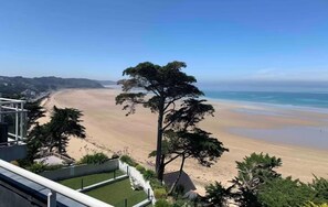 Uitzicht op een strand vanaf een balkon, met een boom op de voorgrond.