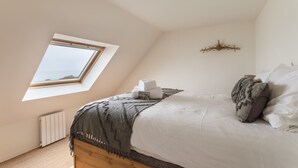 Ein Schlafzimmer mit Dachfenster, einem Bett mit weißen Bettbezügen, einer grauen Decke und einer dekorativen Wandgestaltung.