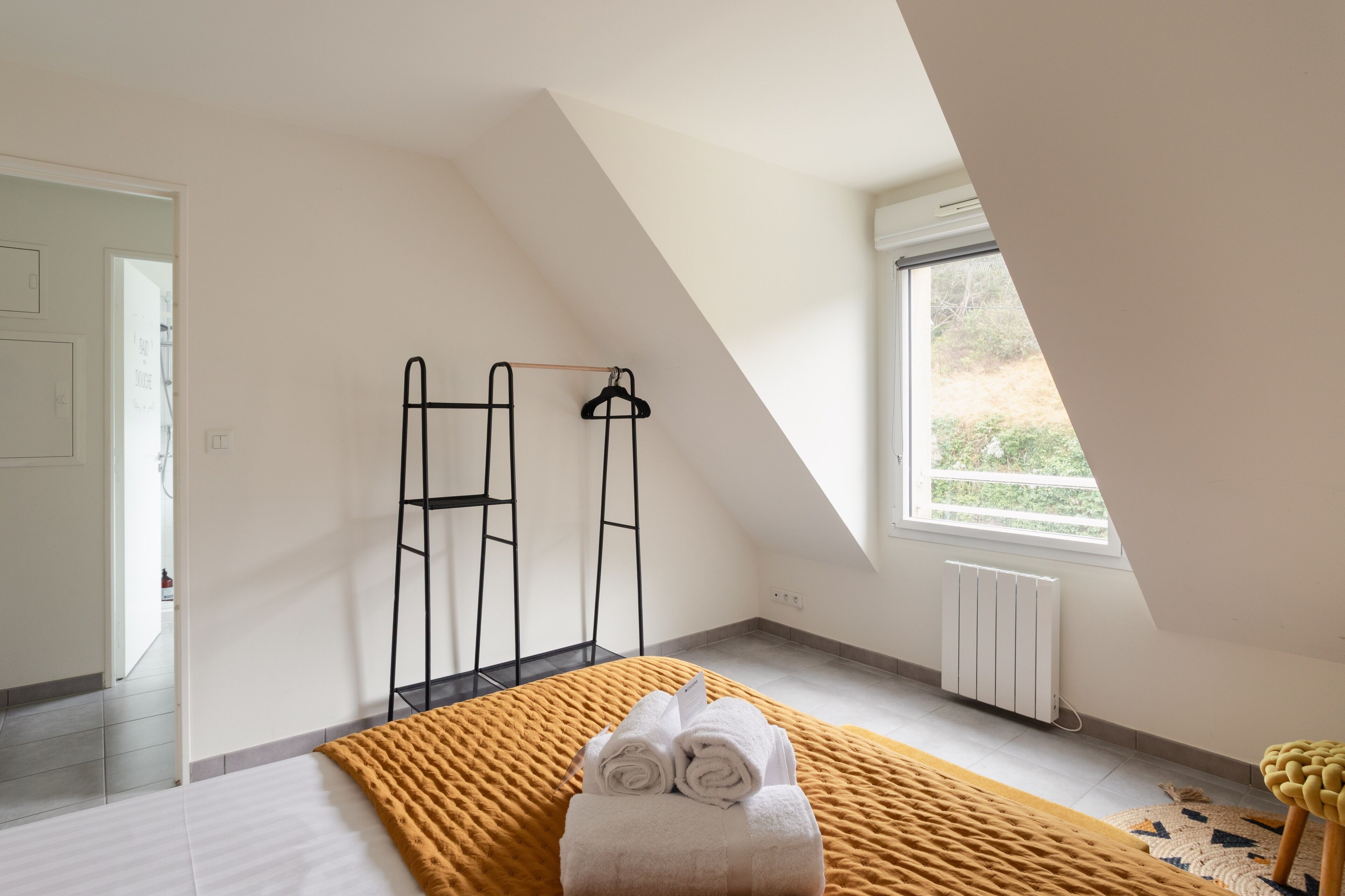 A bedroom with a bed, a window, a radiator, and a towel on the bed.
