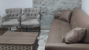 Ein Wohnzimmer mit Steinswand, zwei Sesseln, einer Couch und einem Couchtisch.