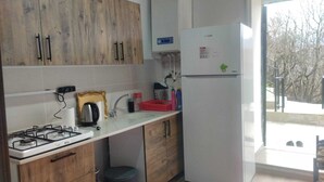 Eine Küche mit Holzschränken, einem Gasherd, einem weißen Kühlschrank und einem Fenster mit Blick auf Bäume.
