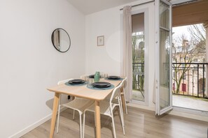 Un coin repas avec une table dressée pour quatre personnes, un miroir au mur et une vue à travers une porte vitrée.