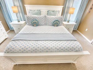 Ein Bett mit gemustertem Überwurf, zwei passende Kissen, ein Nachttisch mit Lampe und ein weiterer Nachttisch ebenfalls mit Lampe.