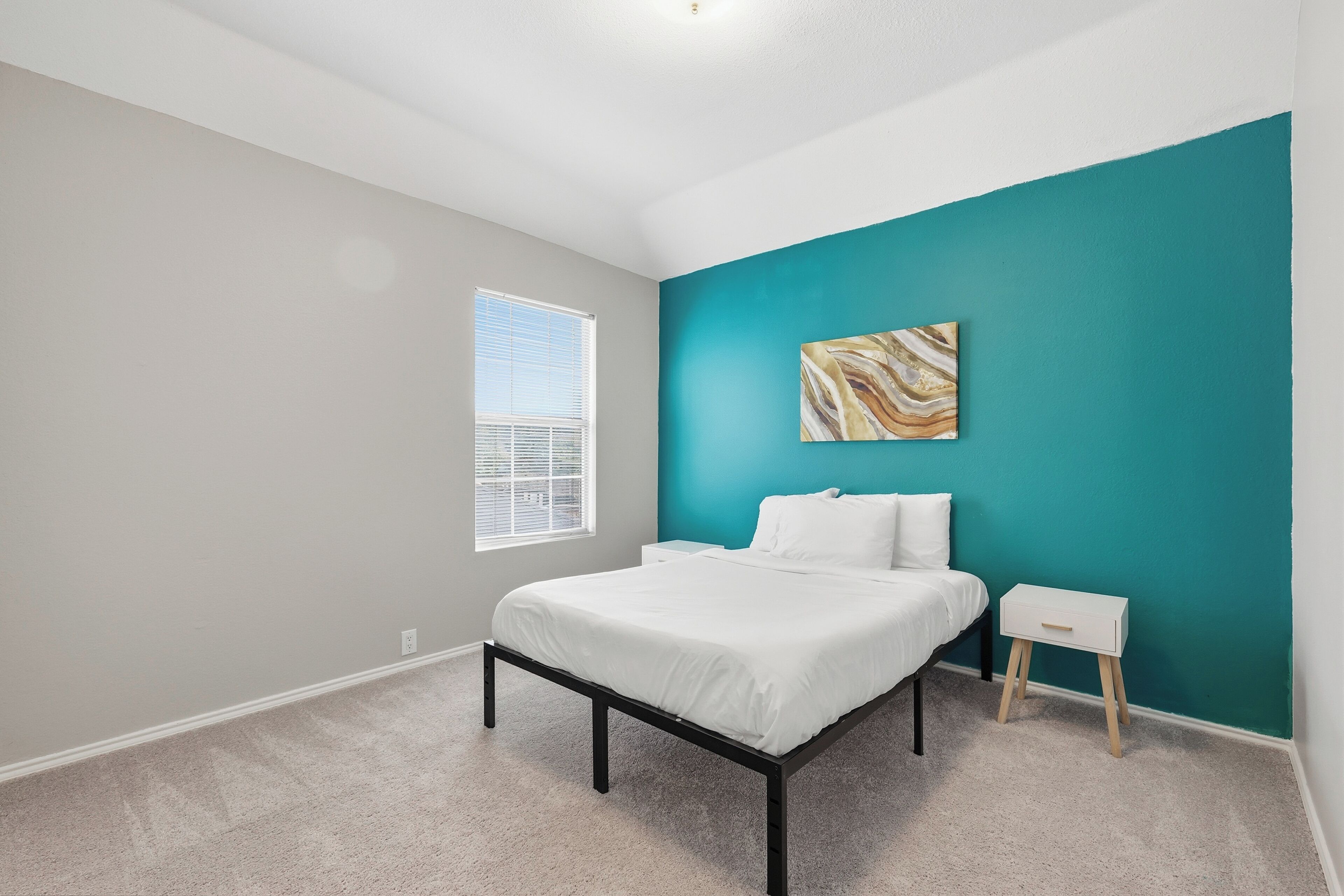 A bedroom with a bed, a nightstand, a window, and a teal accent wall.