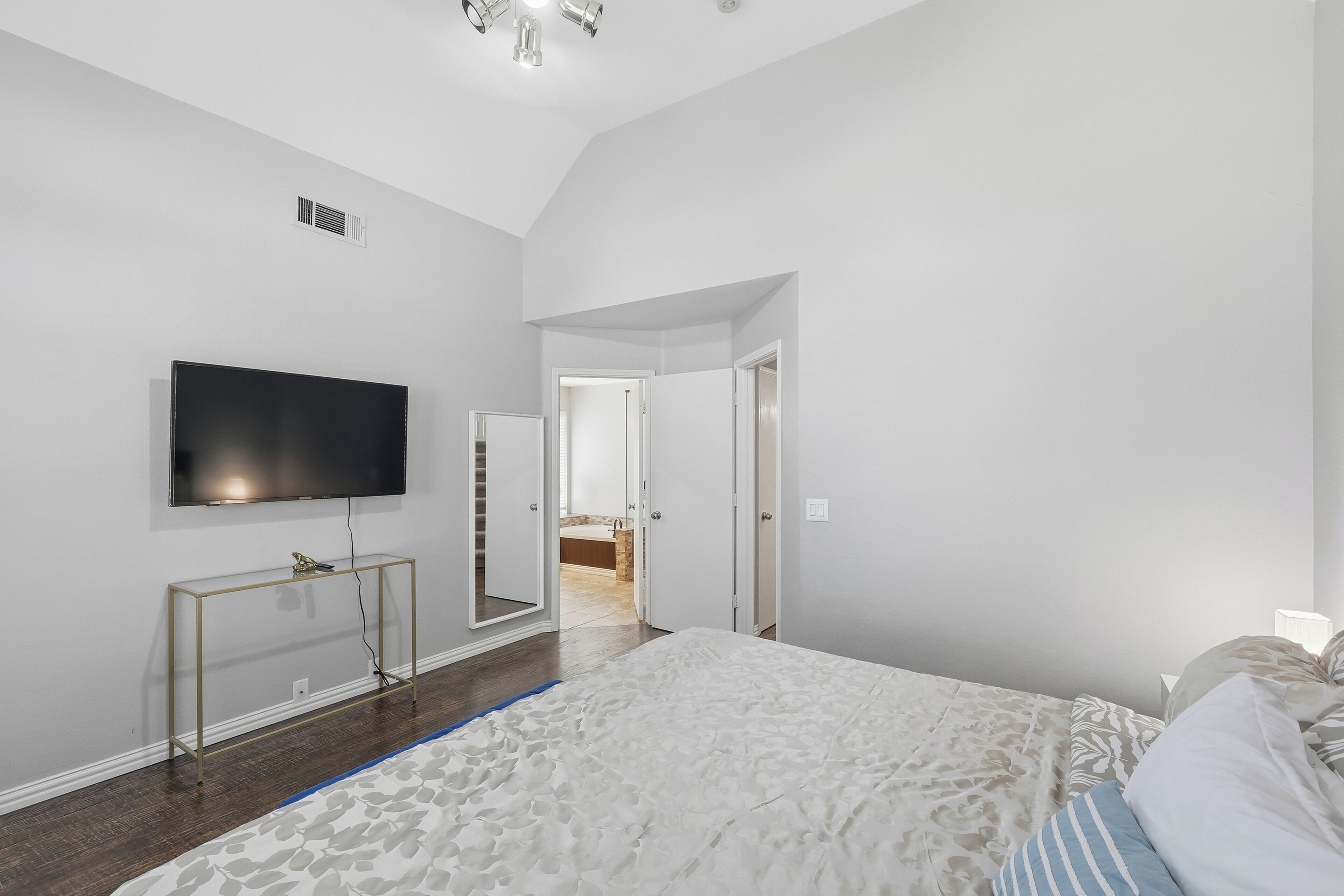 A bedroom with a bed, a TV mounted on the wall, and a door leading to a bathroom.