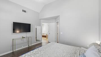 A bedroom with a bed, a TV mounted on the wall, and a door leading to a bathroom.