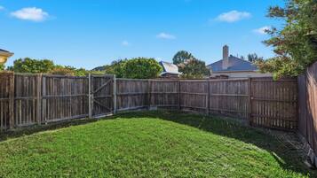 A fenced backyard with a grassy lawn, a wooden gate, and a house in the background.