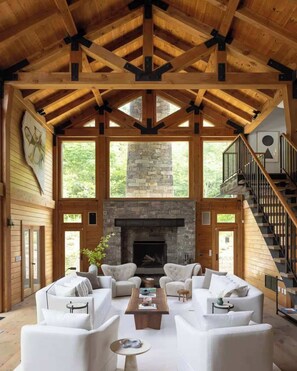 Un salón espacioso con chimenea de piedra, mobiliario blanco y techo de madera.