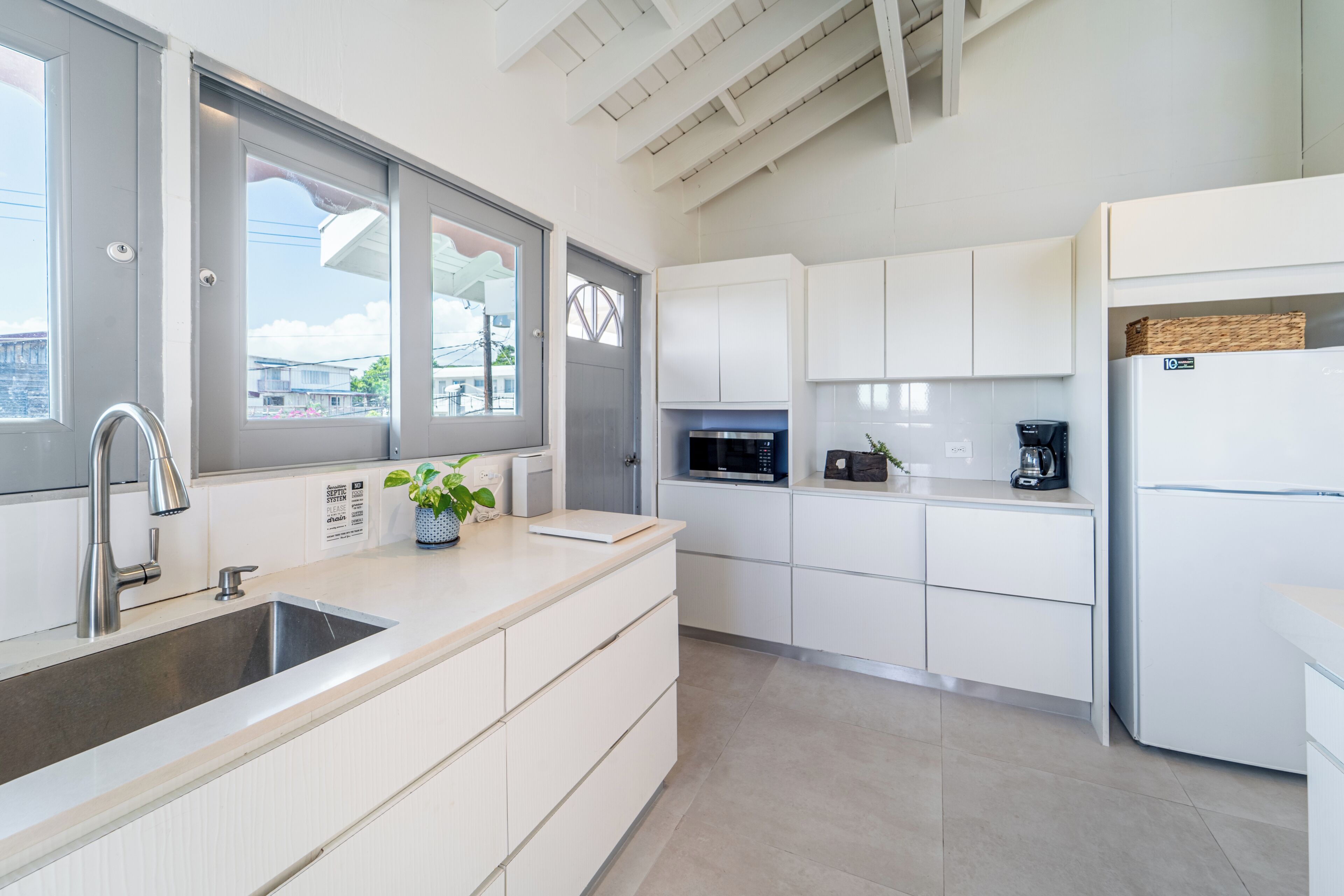A modern kitchen with white cabinetry, a stainless steel sink, a microwave, and a refrigerator.