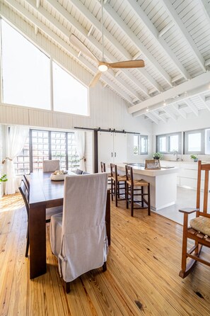 A spacious kitchen with a large island, wooden flooring, and a high ceiling with exposed beams.
