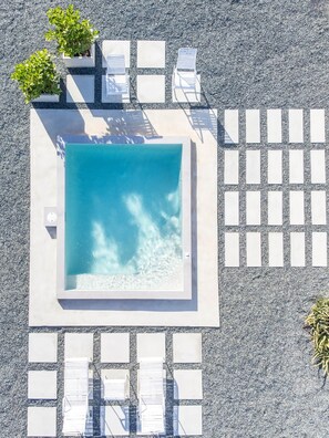 A square pool with clear water, surrounded by white lounge chairs and potted plants.
