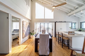 A spacious dining area with a long table, wooden flooring, and a high ceiling with exposed beams.