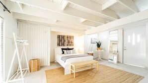 A bedroom with a bed, a wooden bench, a woven rug, a white wardrobe, and a small table with a plant. - My Sandlot Parguera- Beach Chalet up to 16 guests (La Parguera)