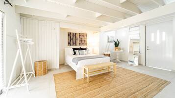 A bedroom with a bed, a wooden bench, a woven rug, a white wardrobe, and a small table with a plant.